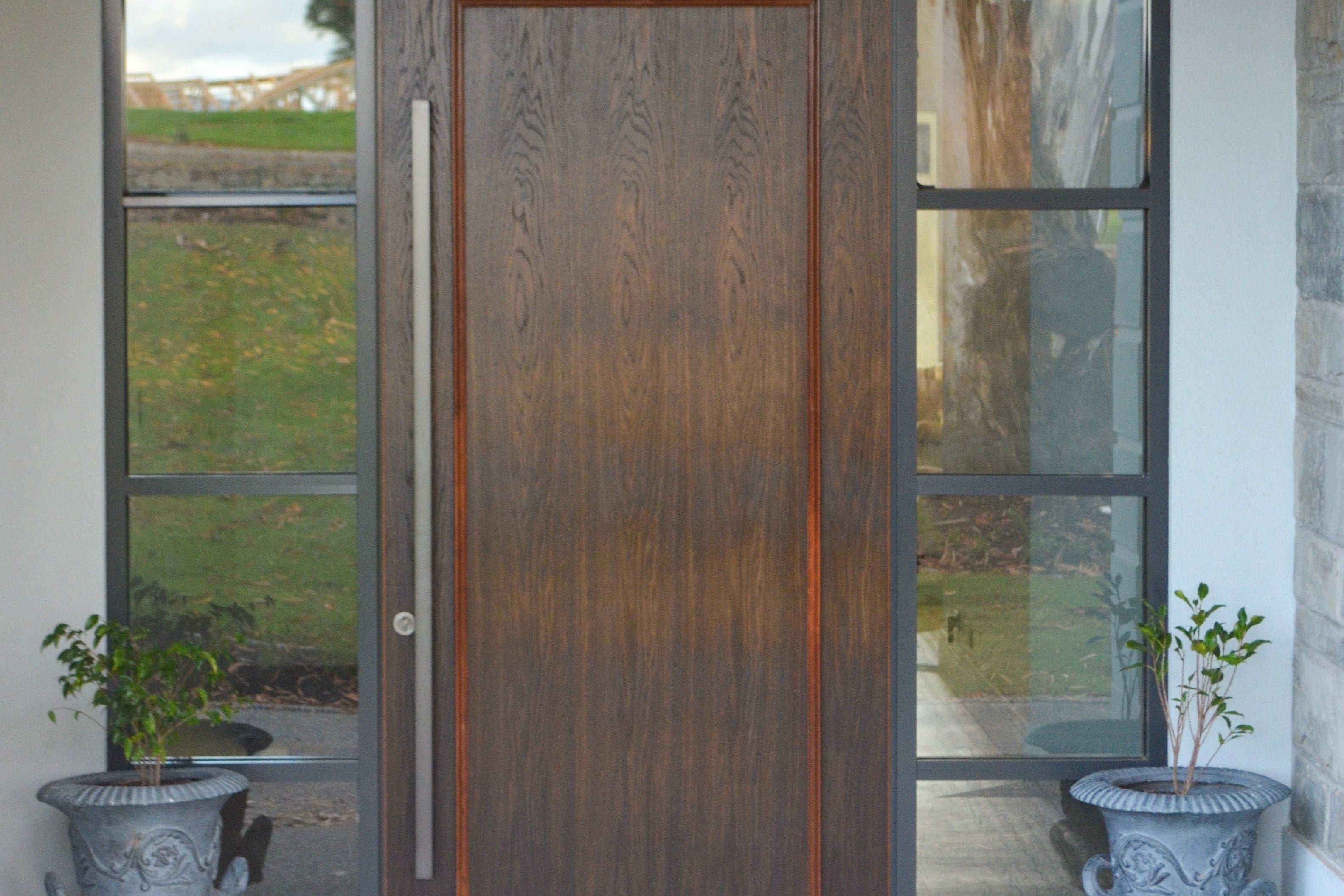 Wooden front door with glass panels and 'HOME' doormat on a stone pathway.