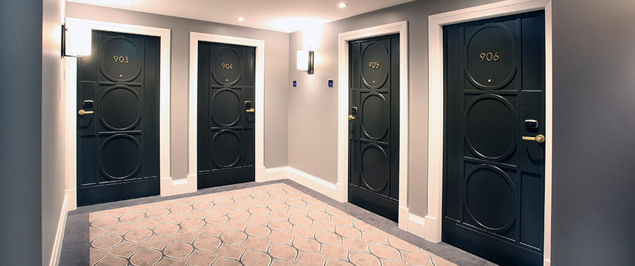 Four black doors with gold handles in a hallway with gray walls and a patterned floor.