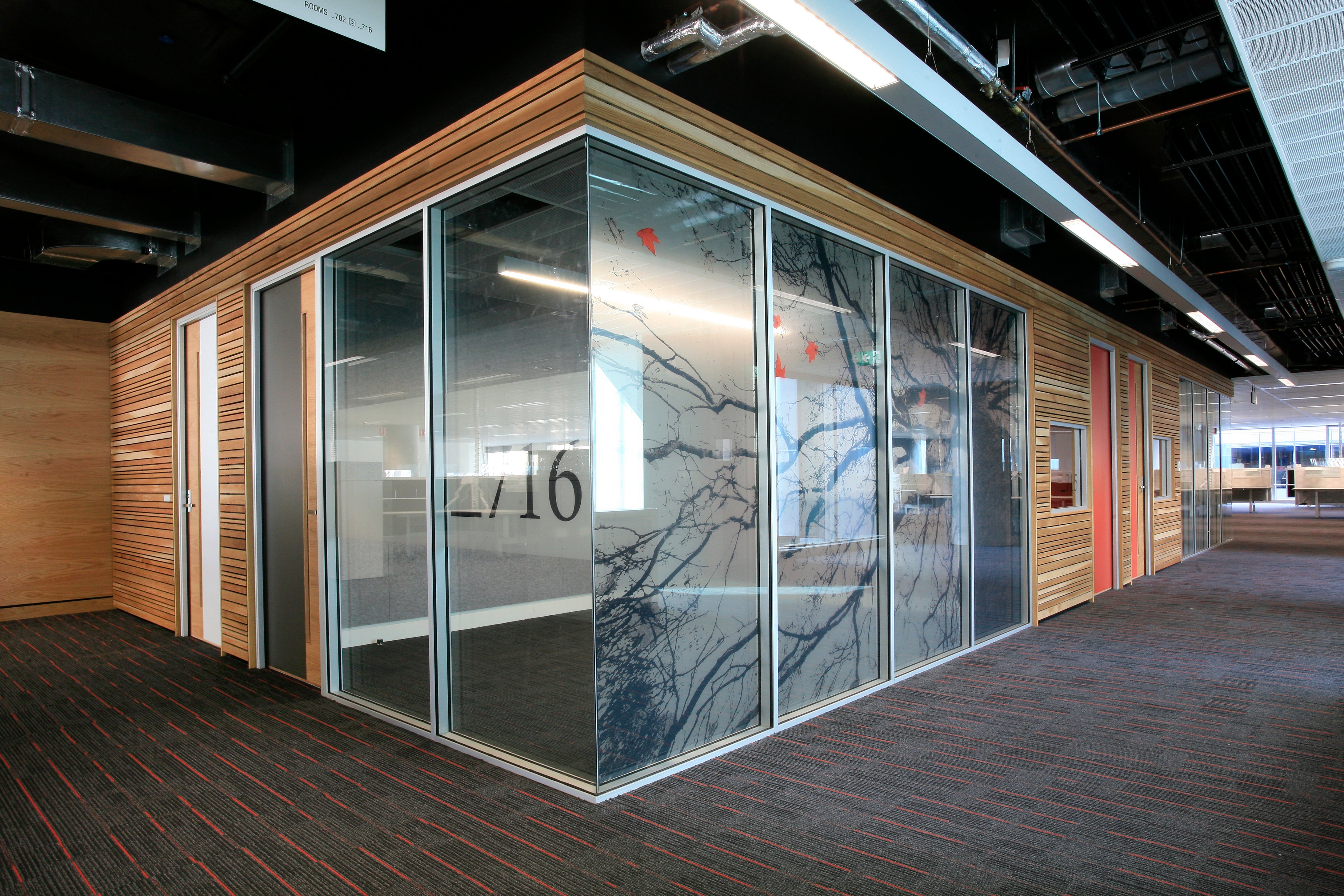 Modern office space with glass-walled partition and wooden panels.