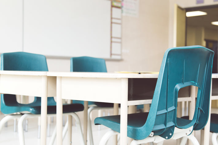Blue chairs at white desk in classroom environment. 