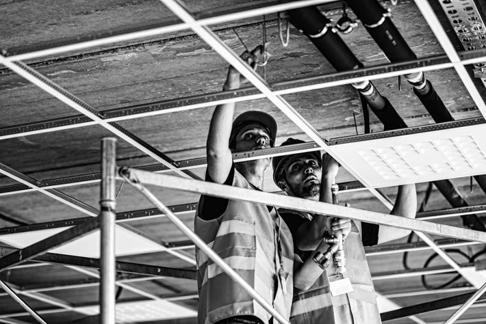 Two workers on a scaffold inspecting ceiling work.
